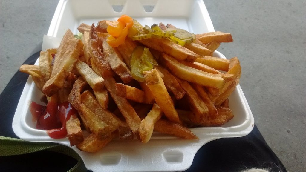 french fries in styrofoam container, topped with hot peppers and a corner with ketchup